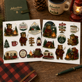 Two Camping Bear Adventure sticker sheets styled on a rustic journaling desk with red plaid and forest-green accessories.