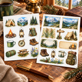 Camping and mountain sticker set on a luxe cabin desk beside a brass pen and green mug
