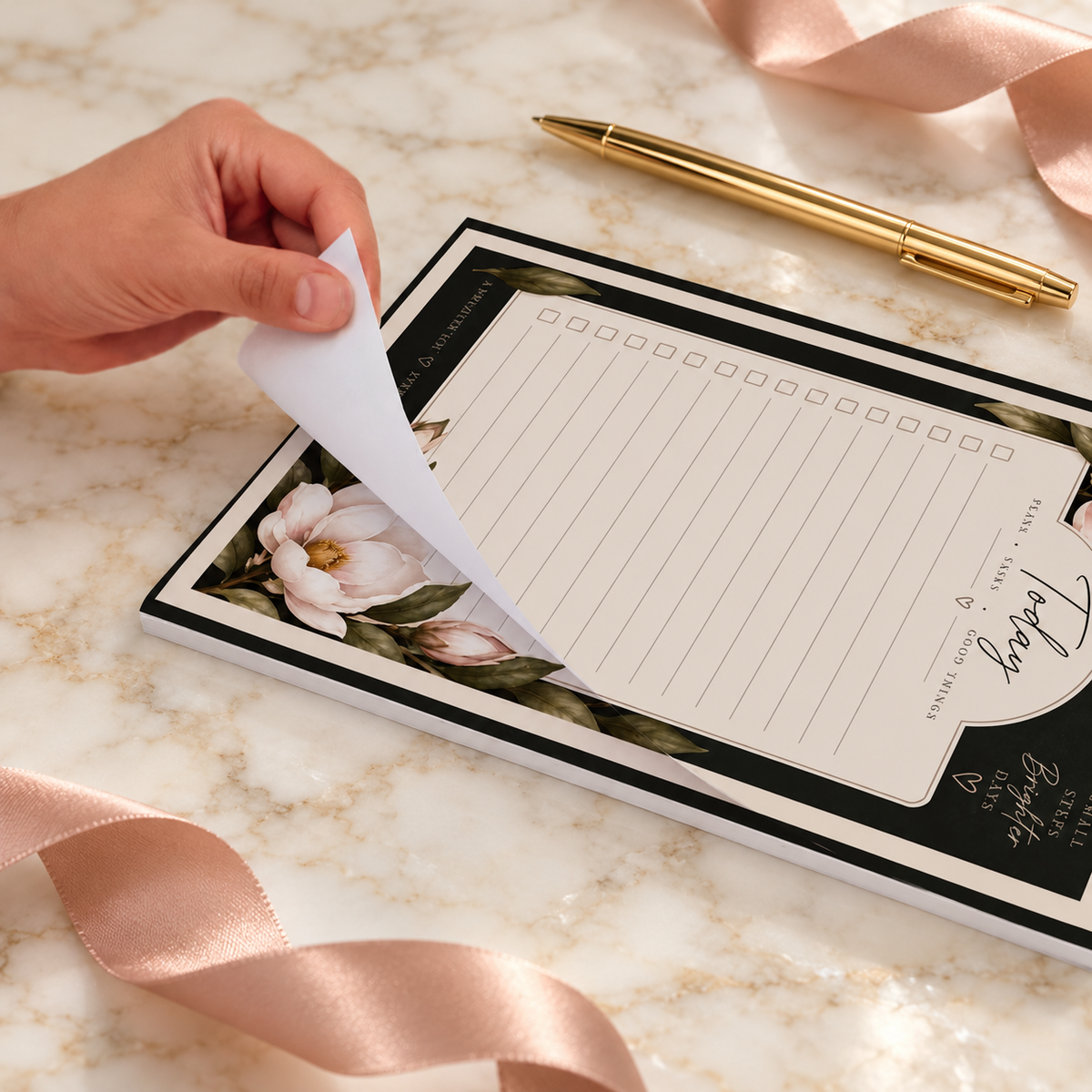 Magnolia Midnight A4 planner pad with a lifted tear-off sheet on ivory marble beside a gold pen and blush ribbon